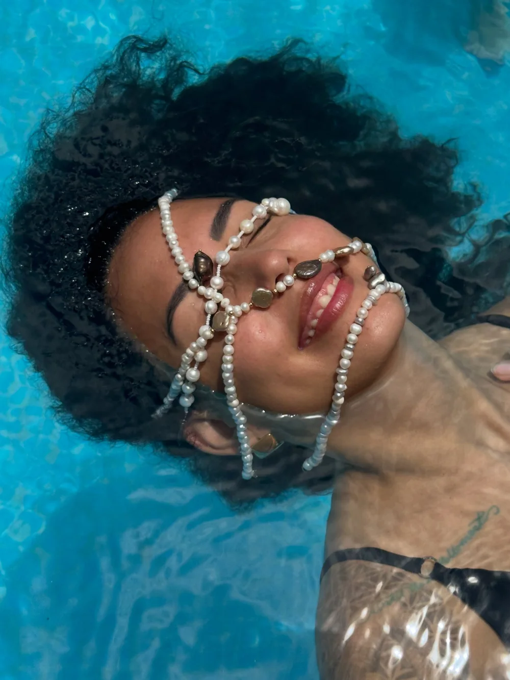 Mujer en el agua con collares de perlas sobre el rostro y el cabello.